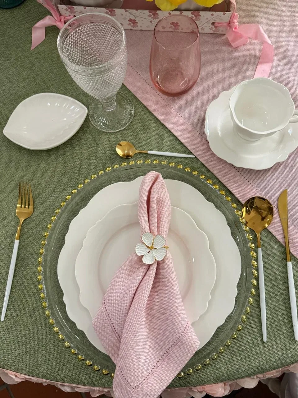 Lugar de mesa con base de perlas doradas, platos Lazio y servilleta rosa con servilletero de flor